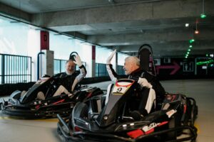 Deux hommes seniors se font un high five en karts, célébrant l'amitié et le plaisir du karting en salle.