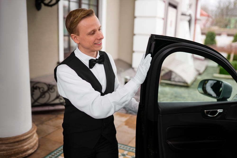 Chauffeur professionnel en tenue formelle ouvrant la portière d'une voiture de luxe pour un service de location avec chauffeur.