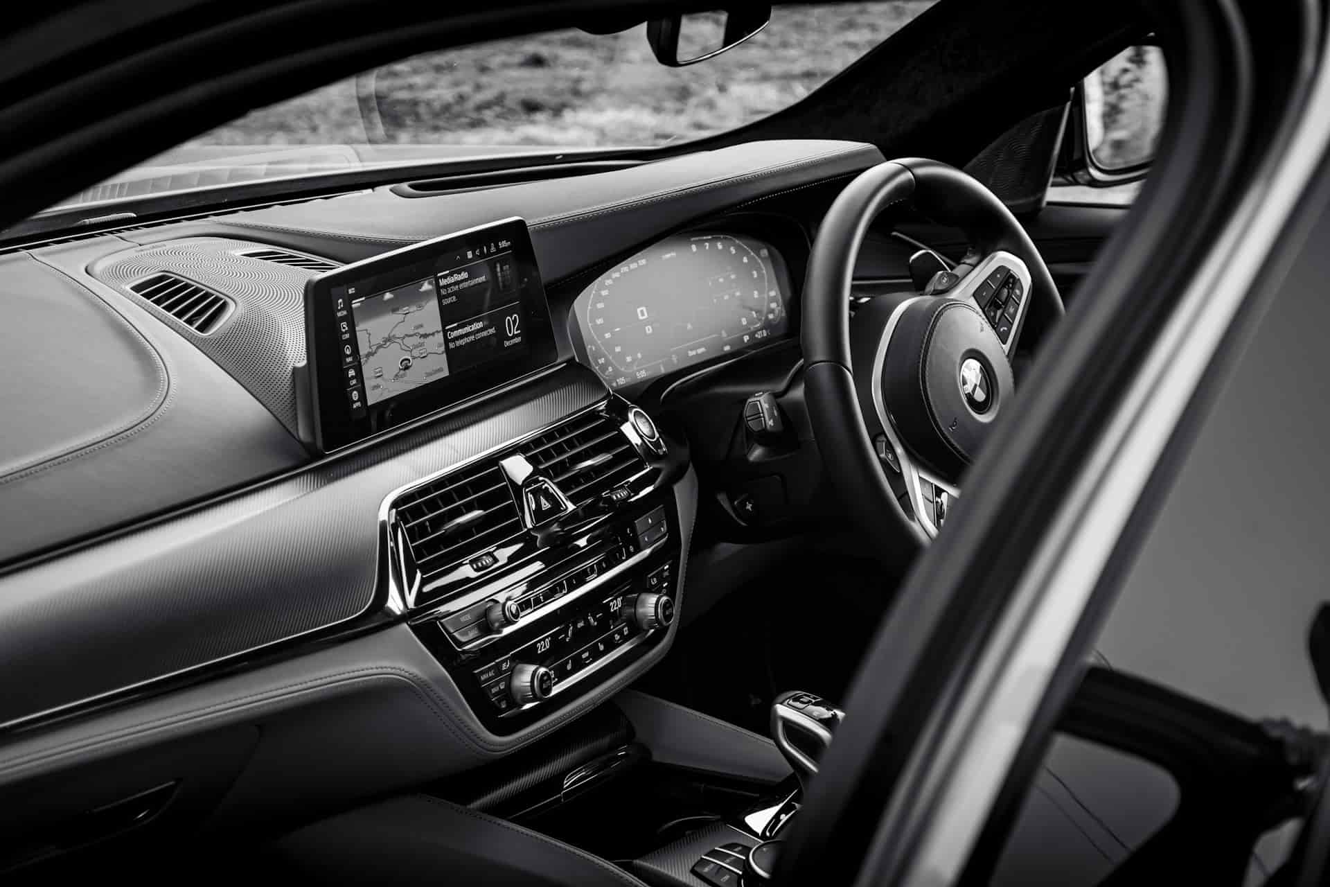 Vue intérieure en noir et blanc d’un tableau de bord moderne d’une BMW Série 5, montrant le volant, le tableau de bord numérique et l’écran d’infodivertissement central avec la navigation active.